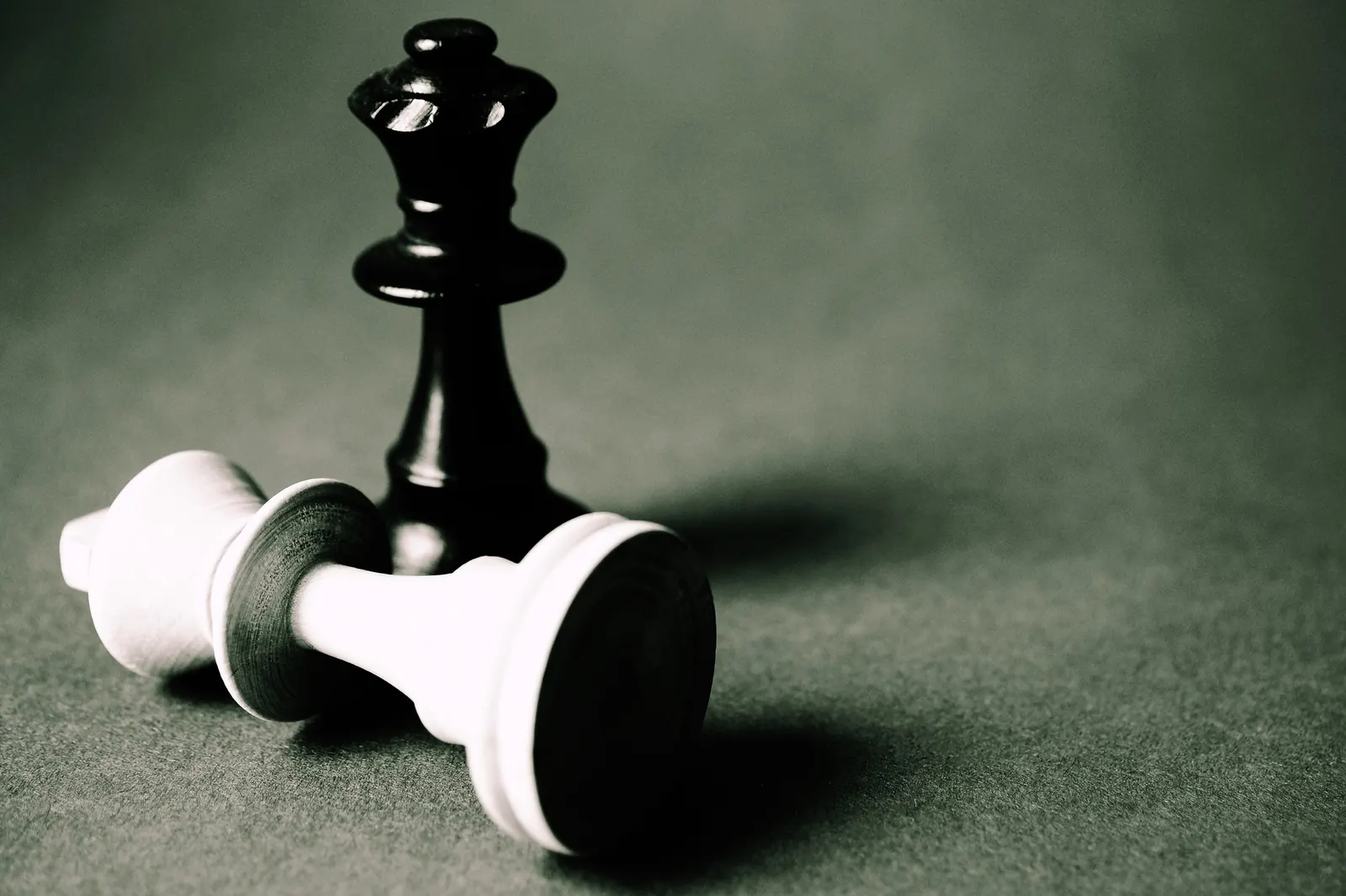 A black chess king topples a white king on a chessboard - a long game, played to win.