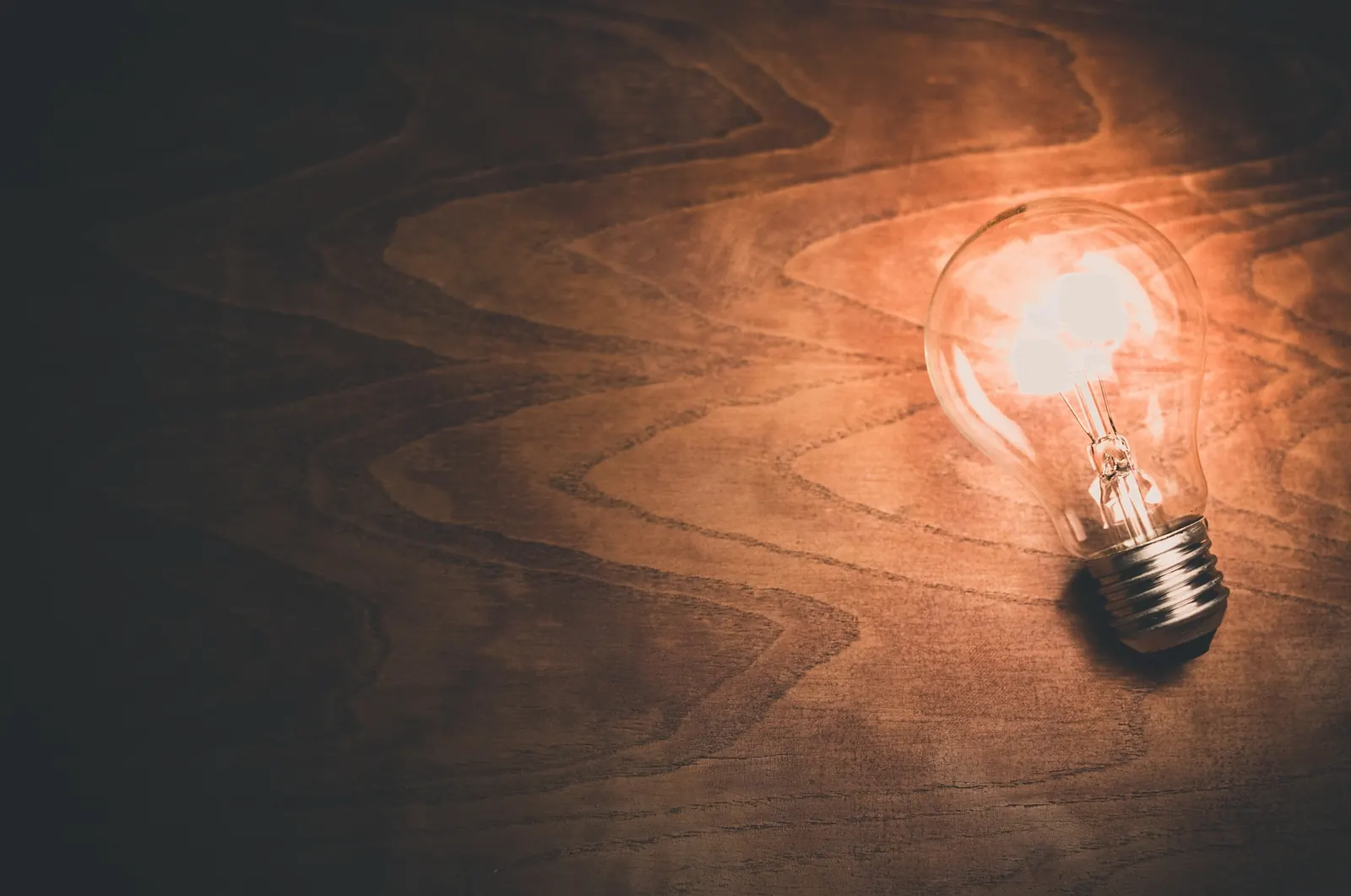 A single glowing light bulb lies on a dark wooden surface - an idea, owned by the person who had it.
